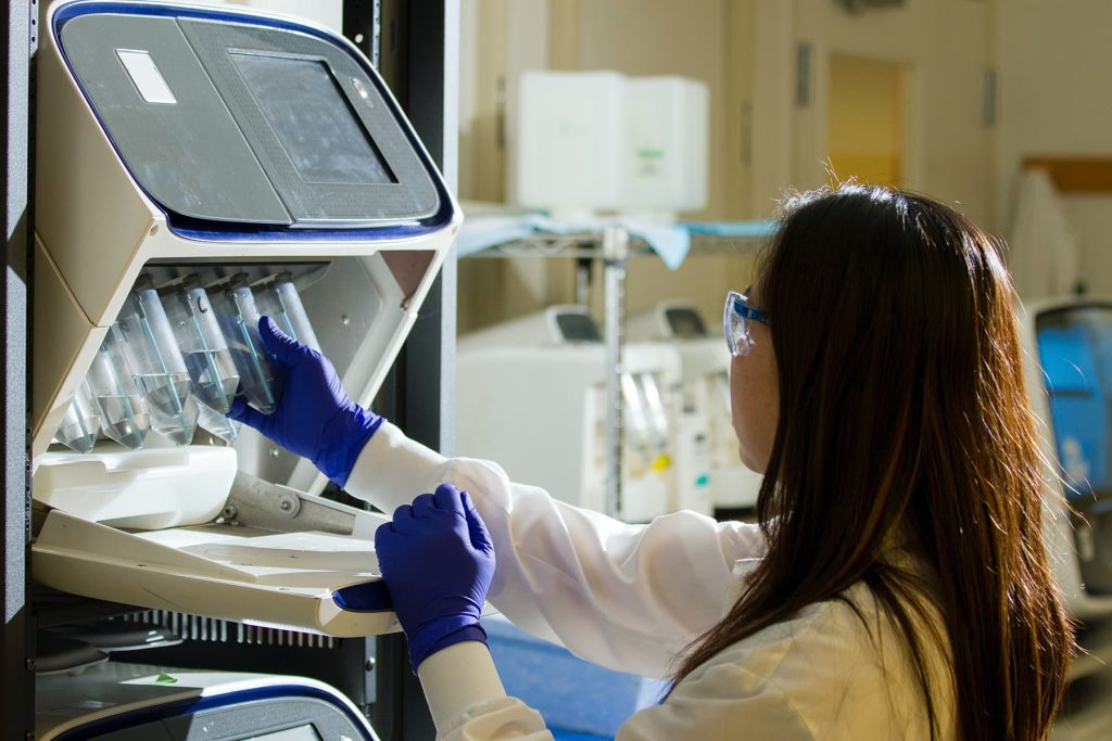 Scientist in safety glasses and gloves loading samples into a laboratory analyzer