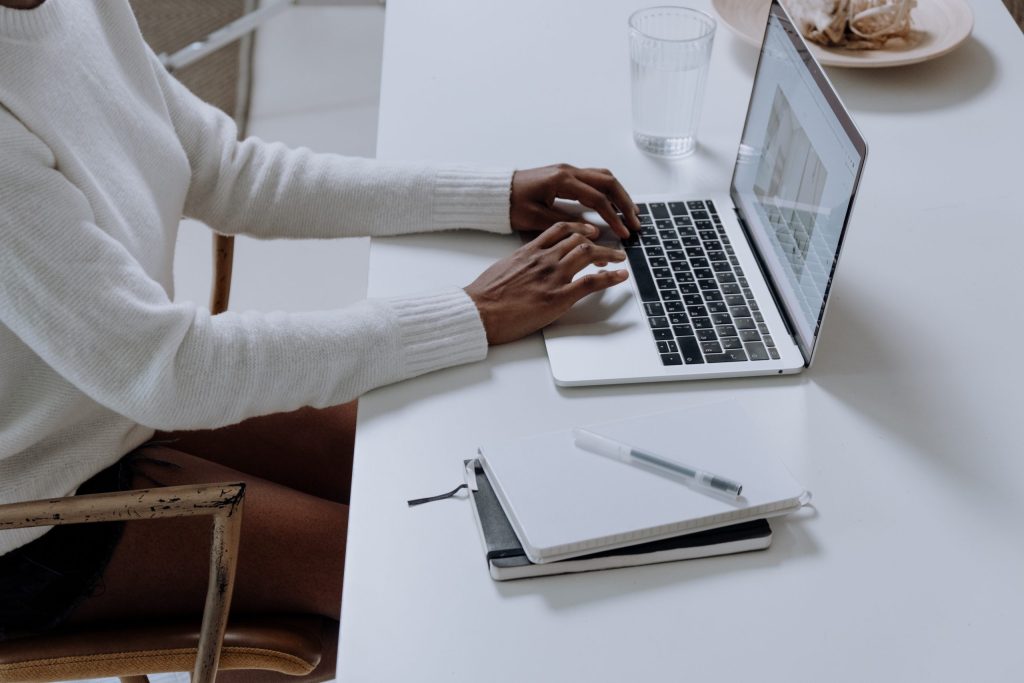 Person typing on a laptop at a table with a notebook and a glass of water