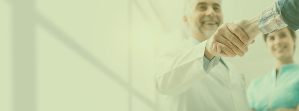 Doctor in a white coat shaking hands with a patient as a nurse smiles nearby