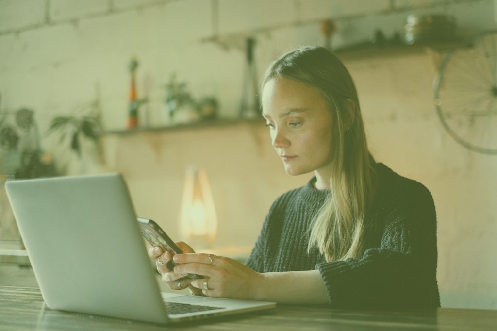 Woman using a smartphone at a desk beside a laptop