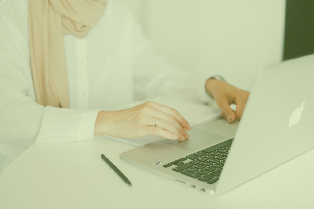 Person wearing a headscarf working on a laptop at a bright desk