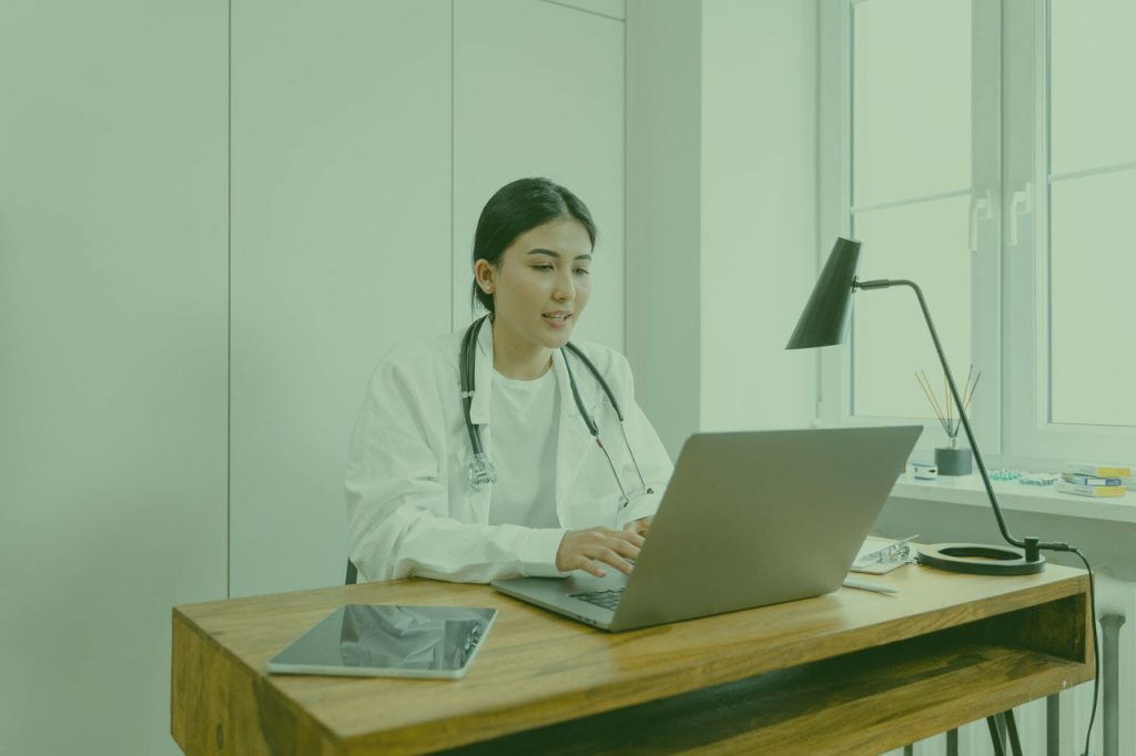 Doctor in a white coat with a stethoscope working on a laptop at a desk