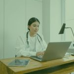 Doctor in a white coat with a stethoscope working on a laptop at a desk